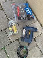 Overall view of Mastercraft electric brad nailer, unopened brad nails, and a red fuel cell tool in packaging placed on stone pavement.