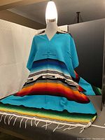Frontal view of the colorful Mexican poncho displayed on a mannequin showing vibrant stripes and V-neck design.