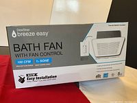 Front side of unopened DewStop Breeze Easy bathroom fan box showing brand, model, features (100 CFM, 1.2 SONE), and mention of included fan control switch.