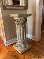Full view of the ornate greenish-grey decorative plinth with classical fluted column and acanthus leaf capitals, sitting on a wood floor.