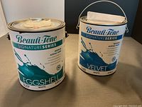 Two unopened metal cans of BeautiTone interior acrylic paint, one Eggshell finish and one Velvet finish, both 3.64 litres, white base. Both cans have handwritten notes taped on top indicating color has not been added.