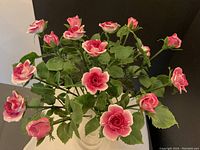 Front view of the full bouquet of 16 pink and white porcelain roses with green leaves arranged inside the glass vase.