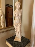 Front and side view of the white marble dust and resin sculpture of a classical female nude torso with cloth draped at the hips, displayed on marble surface with ornate mirror behind.