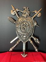 Front view of the metal wall art showing shield with crossed medieval weapons and embossed design.