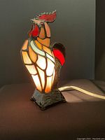 Front-lit view of stained glass rooster lamp illuminated showing warm amber and red light shining through the glass pieces.