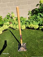 Full view of the garden tamper tool standing on green grass with a 10x10 metal tamping base and wooden handle.