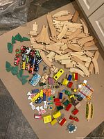 Photo of all wooden train tracks, colorful magnetic train cars, green trees, various road signs, wooden people, and multiple town accessory items spread on the floor.