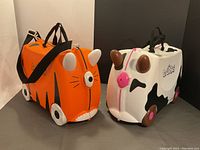 Both Trunki ride-on suitcases side by side, tiger and cow designs