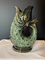 Side view of the green glazed fish-shaped jug showing its curved handle tail and open mouth spout.