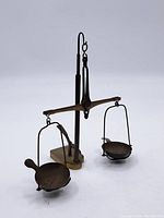 Front angle photo of the antique metal balance scale showing two hanging pans and a vertical stand with hook.