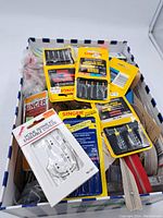 Overall view of box with assorted Singer sewing needles, bobbins, zippers, yarns, and sewing accessories.