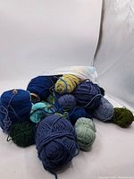 Overall assortment of yarn balls and skeins in blue, green, and yellowish colors showing condition and quantity.