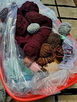 Top view of assorted yarn skeins in different colors placed inside a red plastic bin, partially covered with a plastic bag.