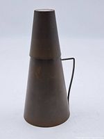 Conical brass pitcher with dark patina, seen from the side, showing narrow top and handle.