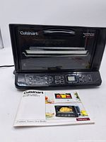 Photo of black Cuisinart convection toaster oven broiler with digital control panel and clear front door on a white surface. Instruction booklet in front.