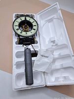 Full clock assembly in styrofoam packaging including clock face, weight, and paper instructions.
