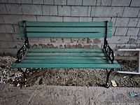 Front view of outdoor bench showing green wooden slats and black metal frame with decorative armrests.