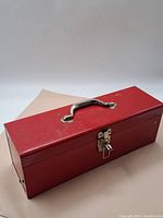 Red metal toolbox closed with silver handle and latch, showing use marks.
