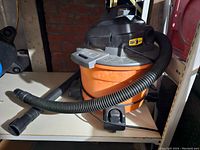 Front side view of orange and black Ridgid shop vac with attached hose and power cord.