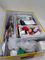 Overhead view of yellow handled box filled with multiple sewing supply items and containers.