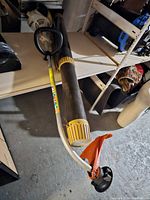 Full length view of Stihl FS 45 strimmer laying on shelf showing handle, shaft, and trimming head.