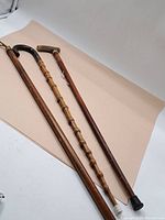 Three vintage walking sticks/canes in various wood styles and designs, displayed with handles and shafts visible.