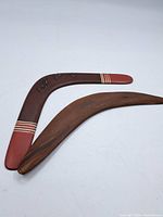 Two boomerangs, one painted brown with red tips and white stripes, the other plain wood with natural finish.