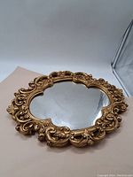 Full view of vintage round mirror with ornate gold frame on neutral background.