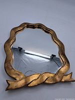 Front view of the vintage giltwood wall mirror showing wavy edges and ribbon motif at the base