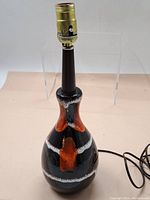 Front view of a glazed ceramic table lamp with black, orange and white glaze and brass socket