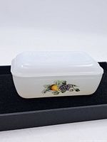 Vintage Pyrex rectangular white/milk glass dish with lid and fruit pattern on sides, placed on black surface.