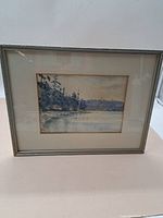 Framed watercolour landscape painting depicting water and trees under glass.