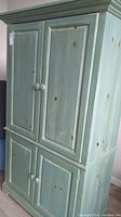 Front and side views of a large distressed wooden cabinet with knots and worn paint in greenish-blue.