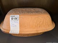 Side view showing decorative carved patterns on the outer surface of the clay baking pan and the MaxSold lot tag.
