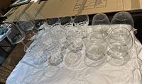 Photo showing 15 assorted crystal glasses arranged on a white cloth, 9 tall stemmed and 6 shorter balloon shaped glasses.