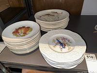 Three stacks of ceramic dinner plates: embossed Royal Cauldon bird/floral design, fruit design plates, and fish design plates.