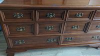 Front view of cherry wood dresser showing nine drawers and ornate metal handles