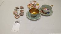 Group shot of three teacup and saucer sets alongside eight miniature oval plates on a white surface.