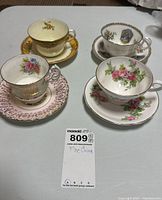 Four fine china tea cups and matching saucers displayed on table showing various floral patterns and gold accents