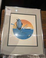 Full view of the matted and framed Indigenous art print showing circular design of loon diving towards a fish with stylized sunset, held under glass.