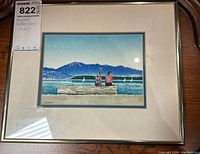 Full view of framed watercolor painting showing two people sitting on a log by a lake with mountains and sailboats in background, with artist signature 'Jacob' visible.