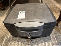 Closed Sentry safe with keys inserted in lock, showing textured dark gray top and silver-gray locking panel with brand and model information.