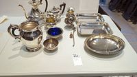 Overview of various electroplated silverware items including trays, bowls, teapots, jugs and more arranged on a white surface