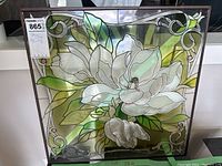 Full view of the square framed stained glass panel showing white flower, leaves and scrollwork