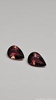Two pear-shaped natural tourmaline gemstones, deep hot pink to purple with clarity VS to VVS, set on a neutral background.