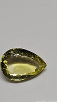 Close-up front view of the pear-shaped lemon citrine gemstone showcasing its bright yellow color, facets, and clarity on plain background.