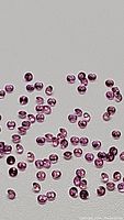 Multiple small round pink sapphires scattered on white background