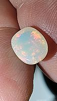 Close-up image showing the cushion cabochon Ethiopian opal with vivid multicolor flashes held between fingers.
