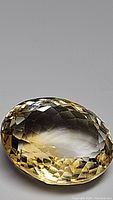 Close-up photo of oval cut natural golden citrine gemstone showing detailed facets and color.