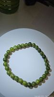Natural green jade stretchy bead bracelet on a white plate, showing varying green shades of round beads.